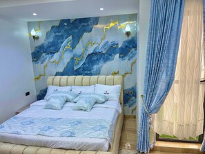 Un dormitorio con cama, pared con diseño tipo mármol y ventana con cortinas.
