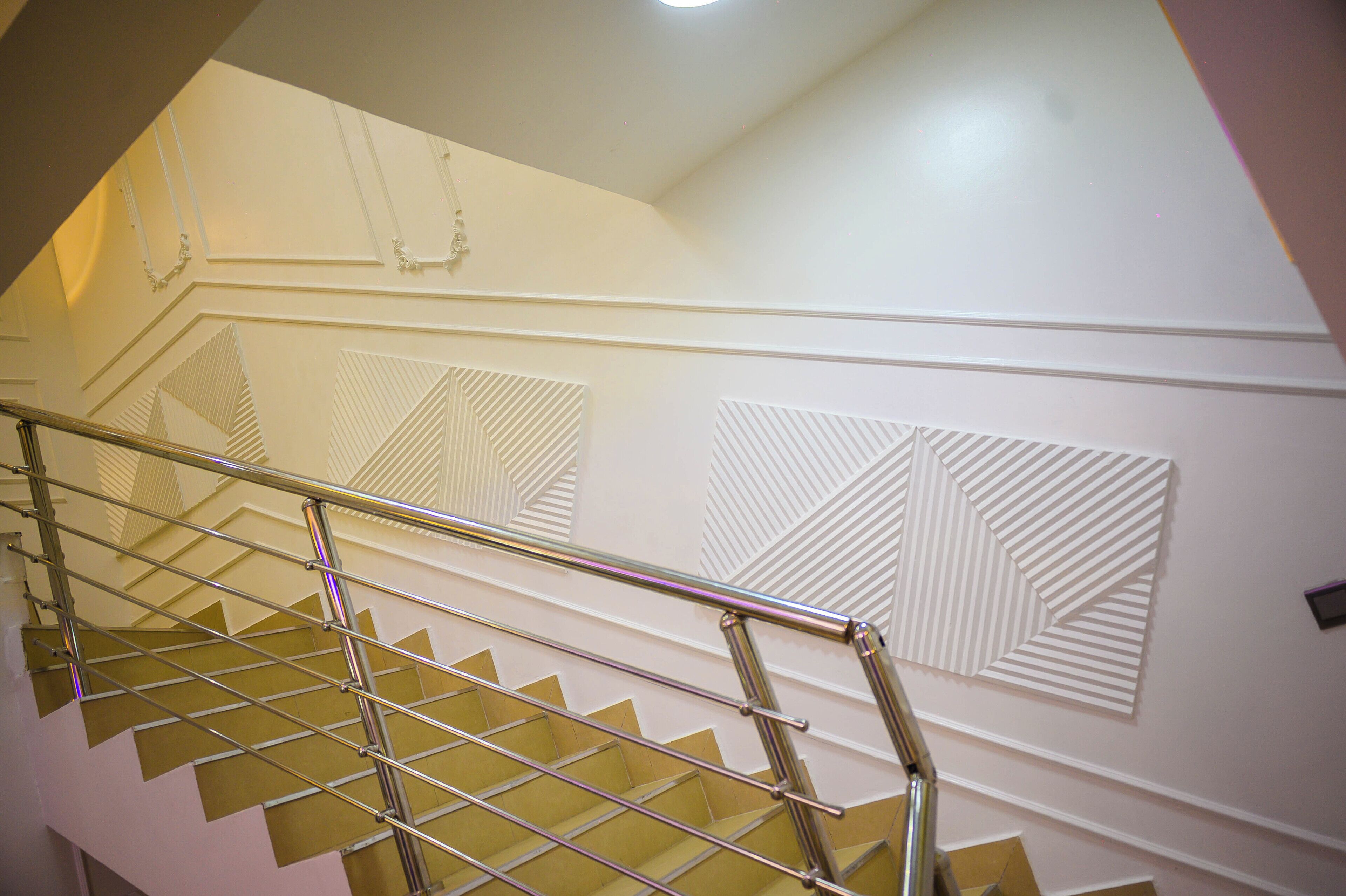 Un escalier doté d’une rampe métallique et de panneaux muraux aux motifs géométriques.