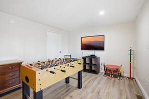 A room with a foosball table, a television, a small table with chairs, and a coat rack. - Working 9 to Pine by Beyond Expectations: Dog Friendly 3BR w/ Views & Game Room (Sevierville)