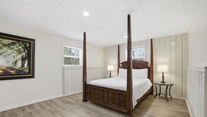 Ein Raum mit Holzboden, weißen Wänden und einem großen, gerahmten Bild, ausgestattet mit einem Himmelbett.