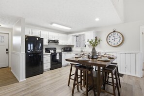 A modern kitchen with white cabinets, a black refrigerator, a dining table set with plates and glasses, and a wall clock. - Working 9 to Pine by Beyond Expectations: Dog Friendly 3BR w/ Views & Game Room (Sevierville)