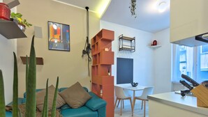 A modern living room with a teal sofa, a dining area with a white table and chairs, and a kitchen with a white countertop and a hanging pot rack. - Le finestre di NoLo, city pad for two in Milan (Milano)