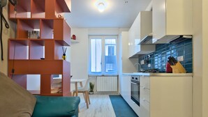 A modern kitchen with white cabinets, a red built-in shelving unit, a blue sofa, and a dining area with a white table and chairs. - Le finestre di NoLo, city pad for two in Milan (Milano)