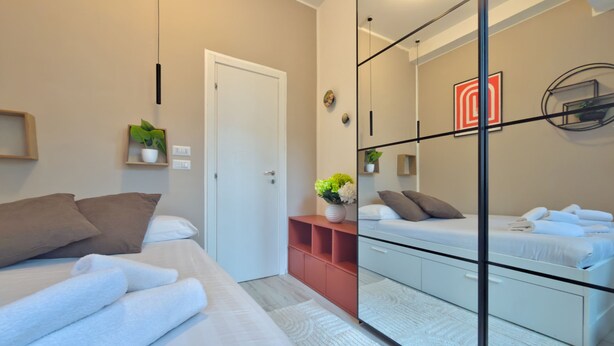 A modern bedroom with a large mirror, a bed with white linens, a red storage unit, and a small plant. - Le finestre di NoLo, city pad for two in Milan (Milano)