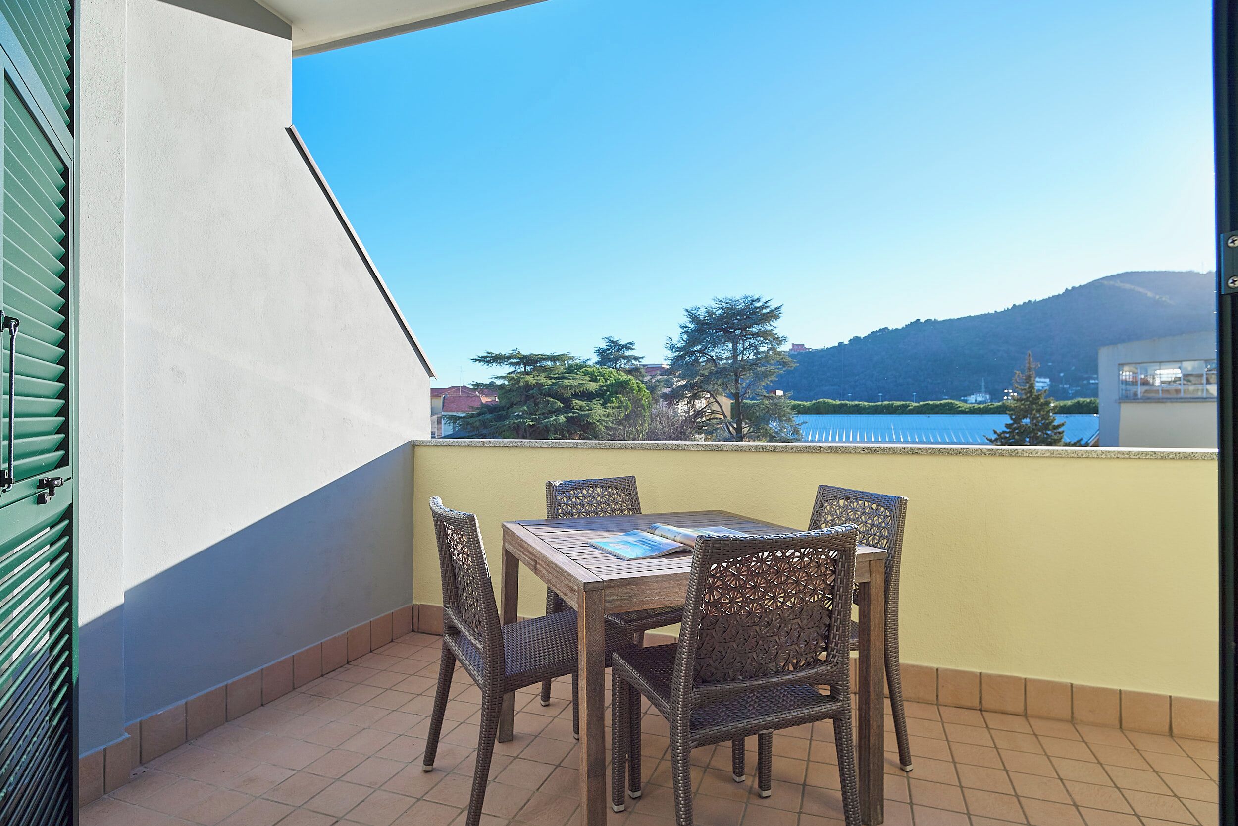 A balcony with a table and chairs, a view of a body of water, and a mountain in the background.