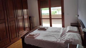 A bedroom with a bed, wooden wardrobe, and a view through a sliding door.
