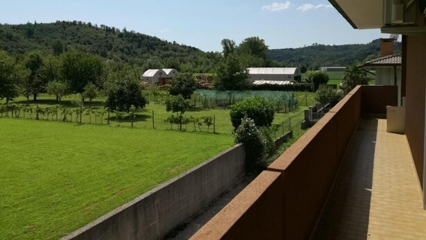 A balcony with a view of a green field, trees, and distant buildings.