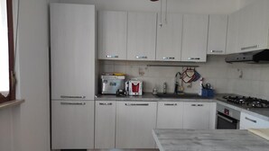 A kitchen with white cabinets, a gas stove, a coffee maker, and a hanging pot rack.