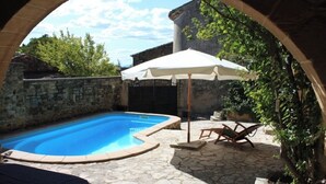 A swimming pool with stone tiles, a white umbrella, and wooden chairs. - Over 1000 year old country house with pool near Uzes for 12 people, ideal for families (Foissac)