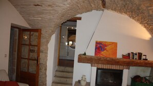 A cozy living room with a stone archway, a fireplace, and a staircase leading to another room. - Over 1000 year old country house with pool near Uzes for 12 people, ideal for families (Foissac)