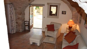 A cozy living room with a white sofa, a chair, a small table, and a lamp. There is a door leading to an outdoor area. - Over 1000 year old country house with pool near Uzes for 12 people, ideal for families (Foissac)