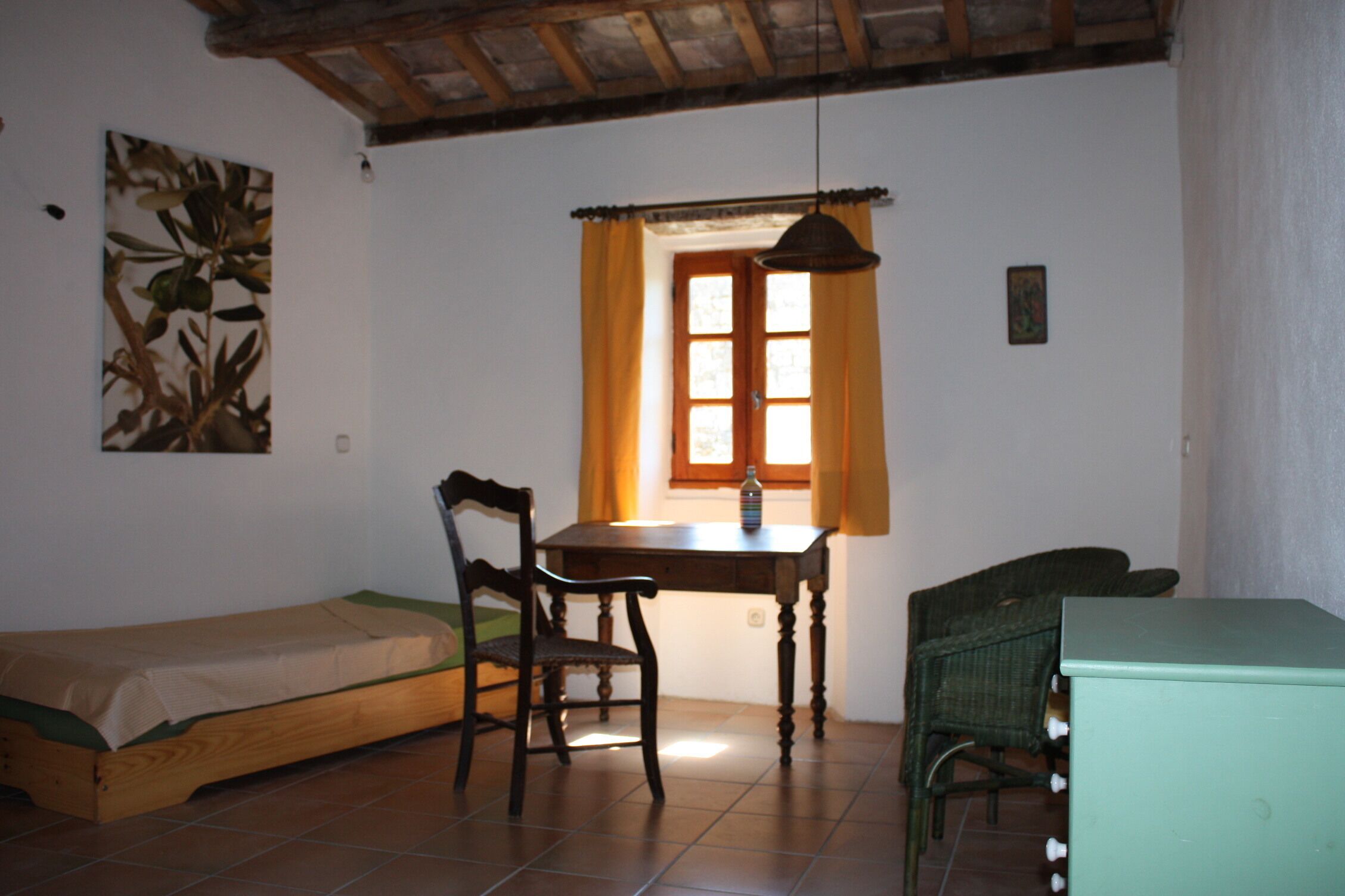 Une petite pièce agréable et chaleureuse, avec un lit, une table en bois, une chaise et une fenêtre avec des rideaux.