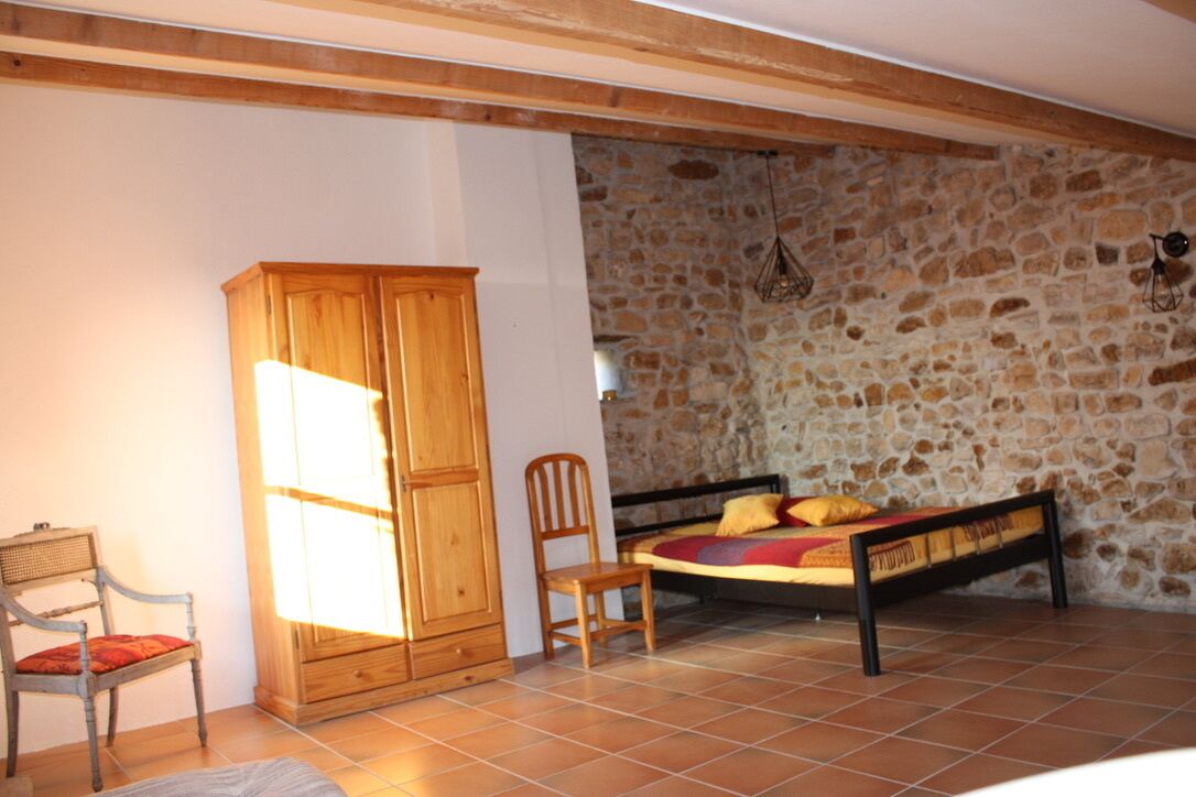 A bedroom with a stone wall, a wooden wardrobe, a bed with a headboard, and a chair.