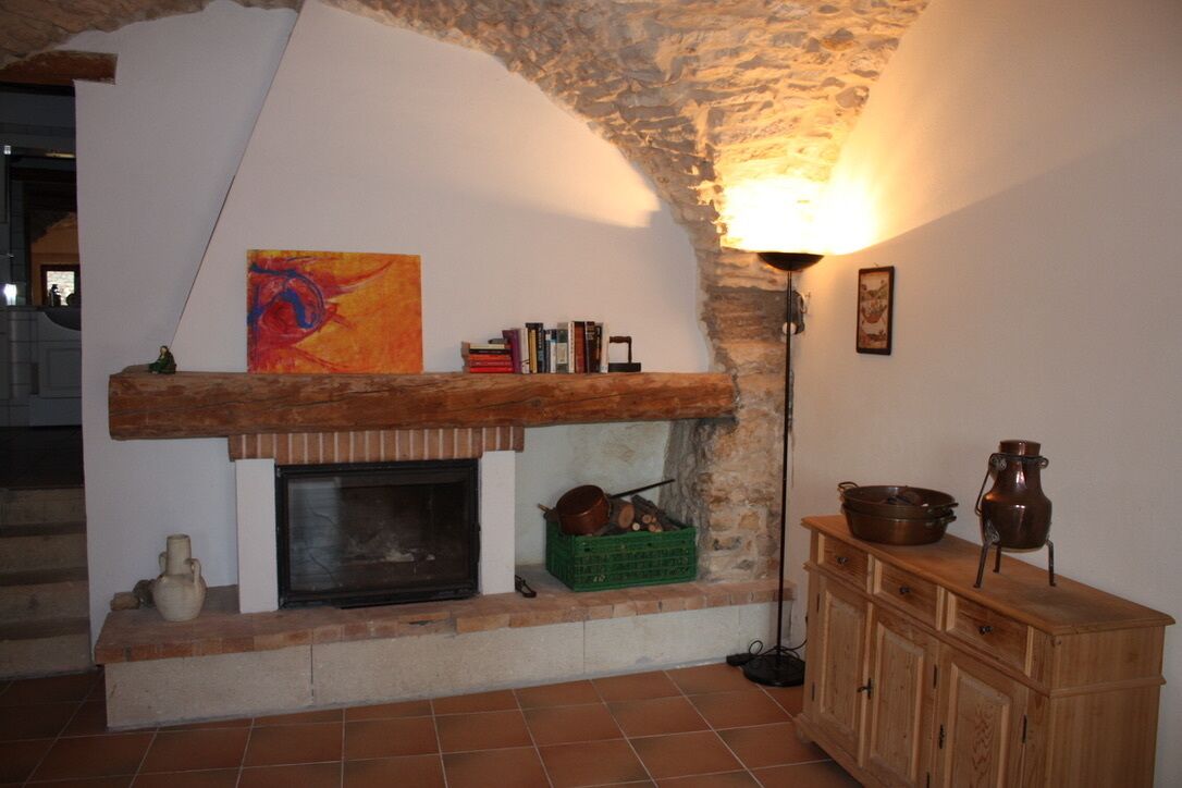 A rustic room with a stone arch, a fireplace, a wooden cabinet, and a painting on the wall.