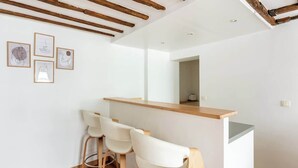 Uma cozinha moderna com armários brancos, bancada de madeira e um espaço bar com dois bancos brancos.
