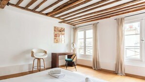Quarto de hotel com cama, escrivaninha, cadeira e janela com cortinas.