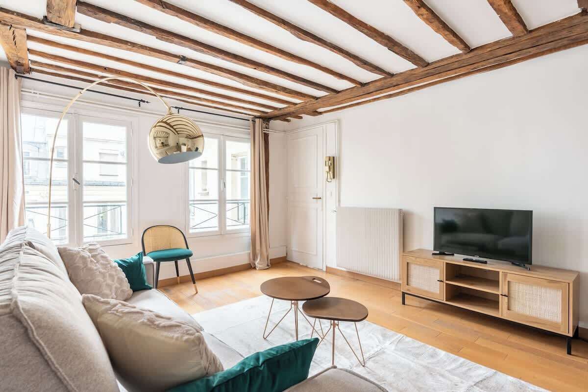A living room with a sofa, two chairs, a TV on a wooden cabinet, and a large window with curtains.