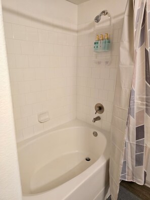 A bathroom with a white bathtub, a showerhead, and a towel rack with toiletries. - LUXURY 1-bedroom apartment in superb Frisco near Toyota Stadium. (Frisco)
