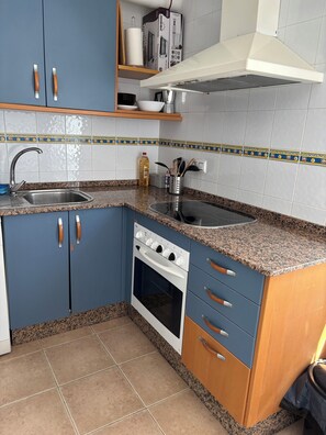 A kitchen with blue cabinets, a stainless steel sink, a stove, and a microwave. There is a shelf above the sink with a box and a bottle. - Seasonal Rental at 80 meters from the beach in Barbate, Cadiz (Barbate)