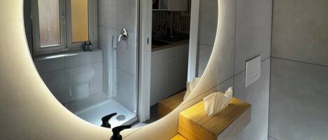 A modern bathroom with a circular mirror, a wooden vanity, a hand soap dispenser, and a towel on the counter.