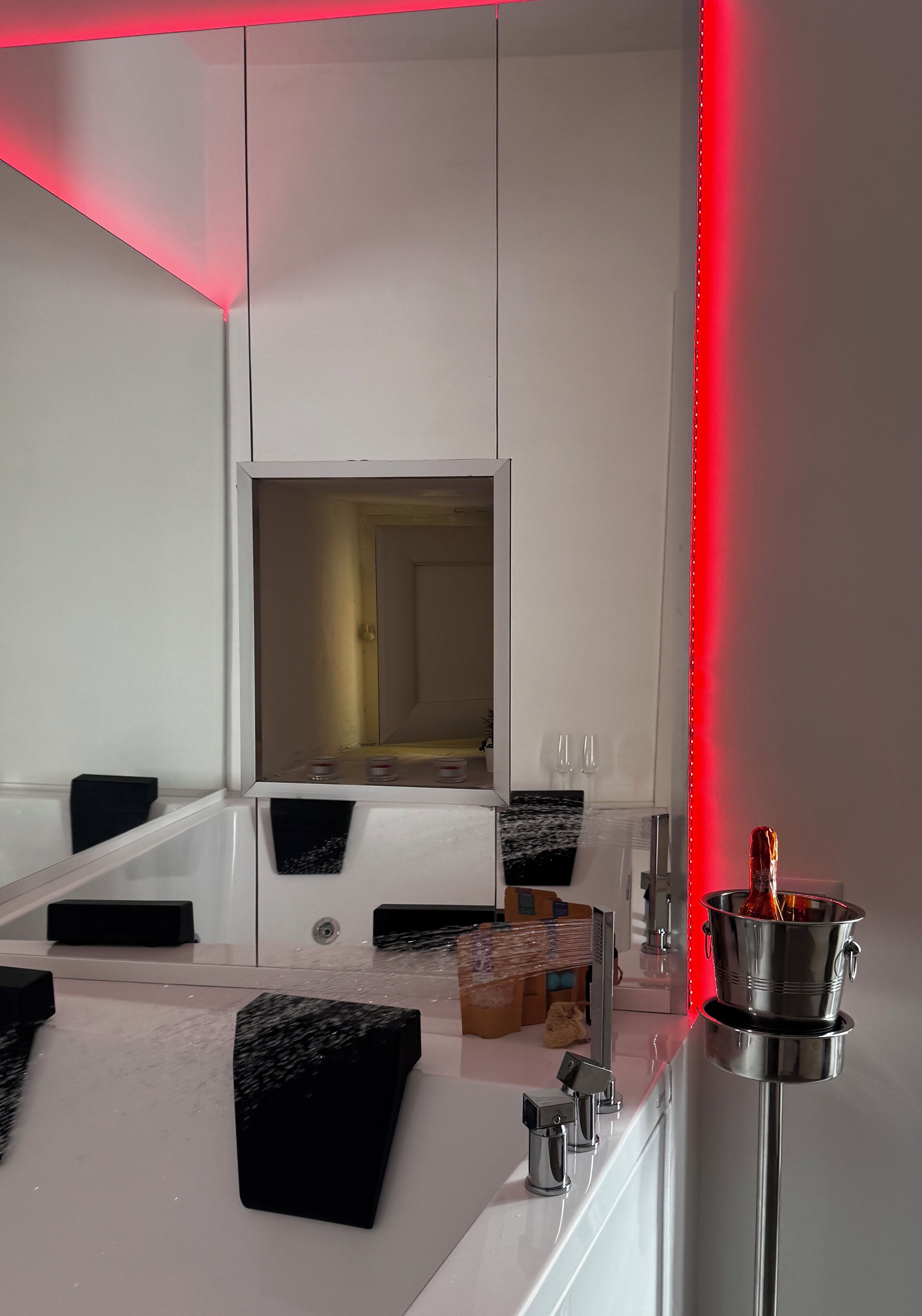 A modern bathroom with a large mirror, a white sink, black soap dishes, and a red LED light strip.