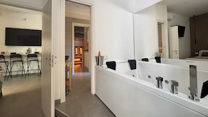 A modern bathroom with a large mirror, a bathtub, and a shower area. There is a door leading to a kitchen area with a dining table and chairs. - Scugnizzo Apartment (Naples)