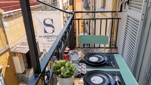 A small outdoor balcony with a table set for two, a potted plant, and a sign for 'Scugnizzi Smart'. - Scugnizzo Apartment (Naples)