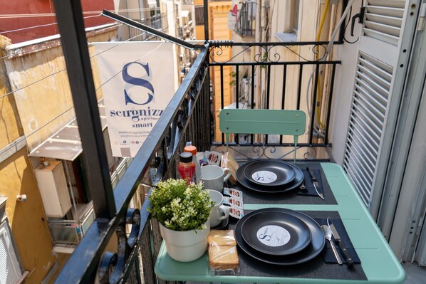 A small outdoor balcony with a table set for two, a potted plant, and a sign for 'Scugnizzi Smart'. - Scugnizzo Apartment (Naples)