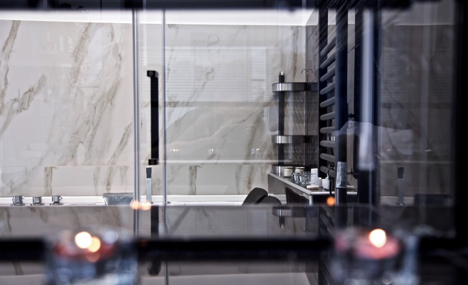 Un baño moderno con baldosas de mármol, mampara de vidrio y zona de lavamanos visible.