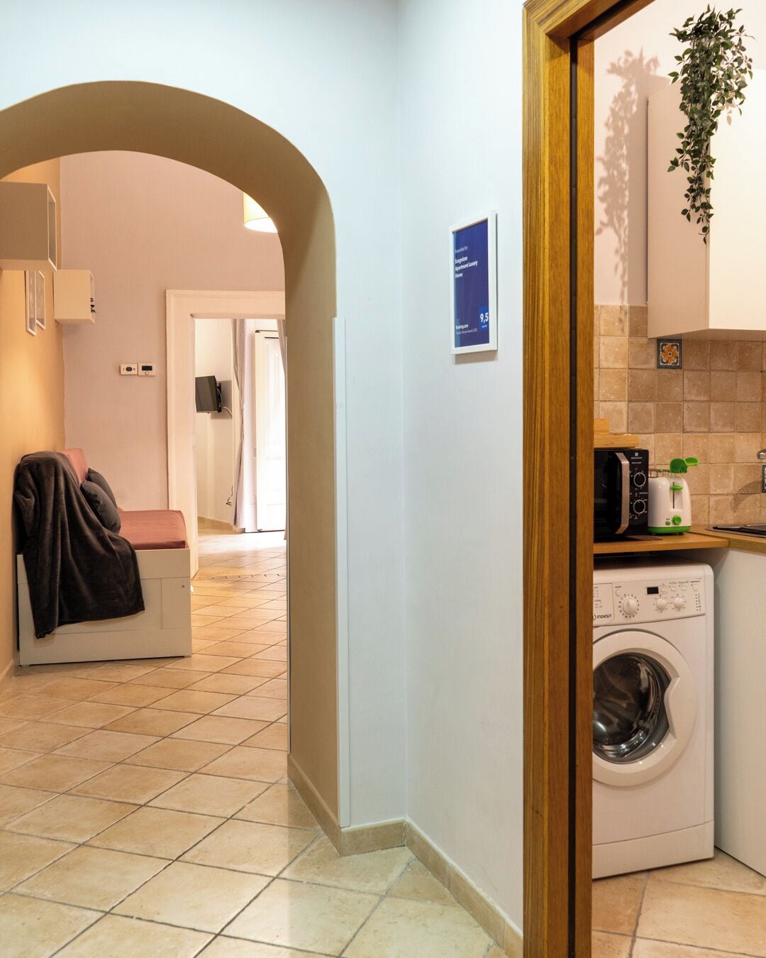 A modern kitchen with a washing machine, a microwave, and a sink. There is a sign on the wall and a plant hanging above the sink.