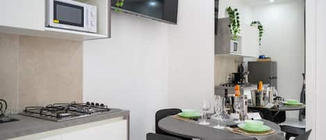 A modern kitchen with a gas stove, microwave, and a flat-screen TV. There is a dining table set with green plates and wine glasses.
