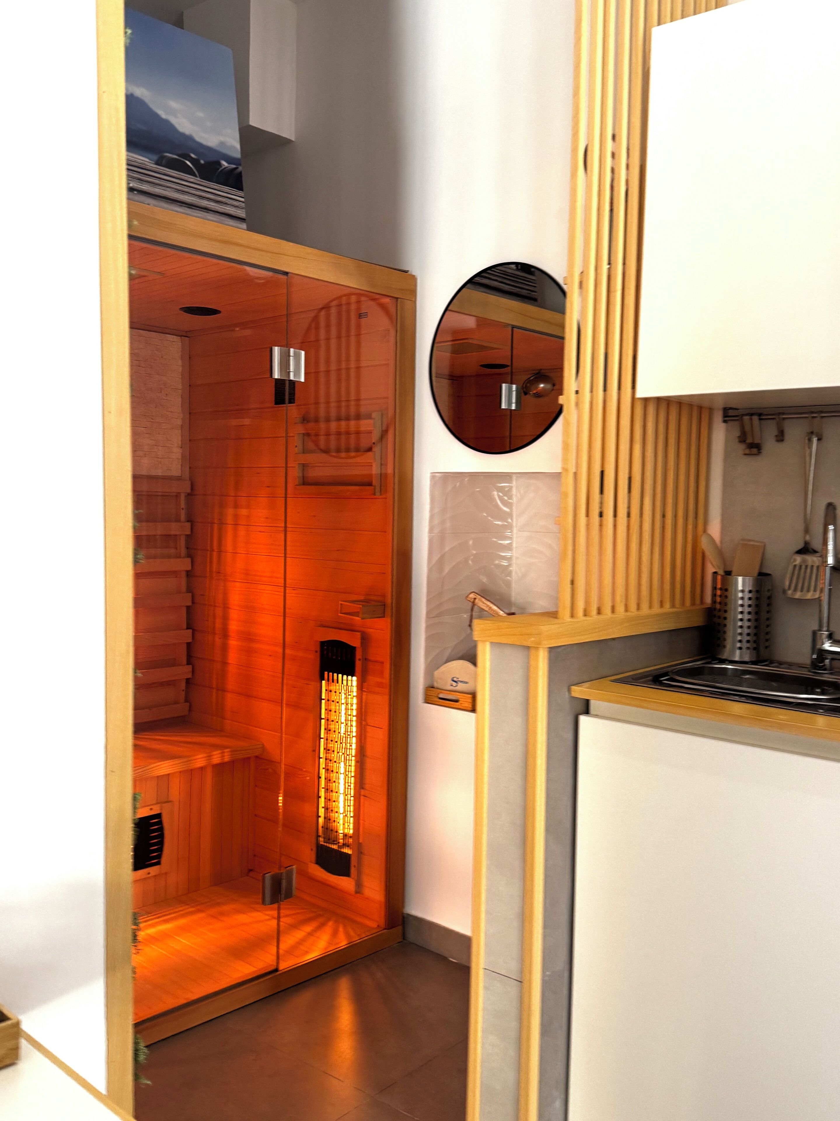 A sauna with a wooden interior, a mirror, and a kitchen area with a sink and utensils.