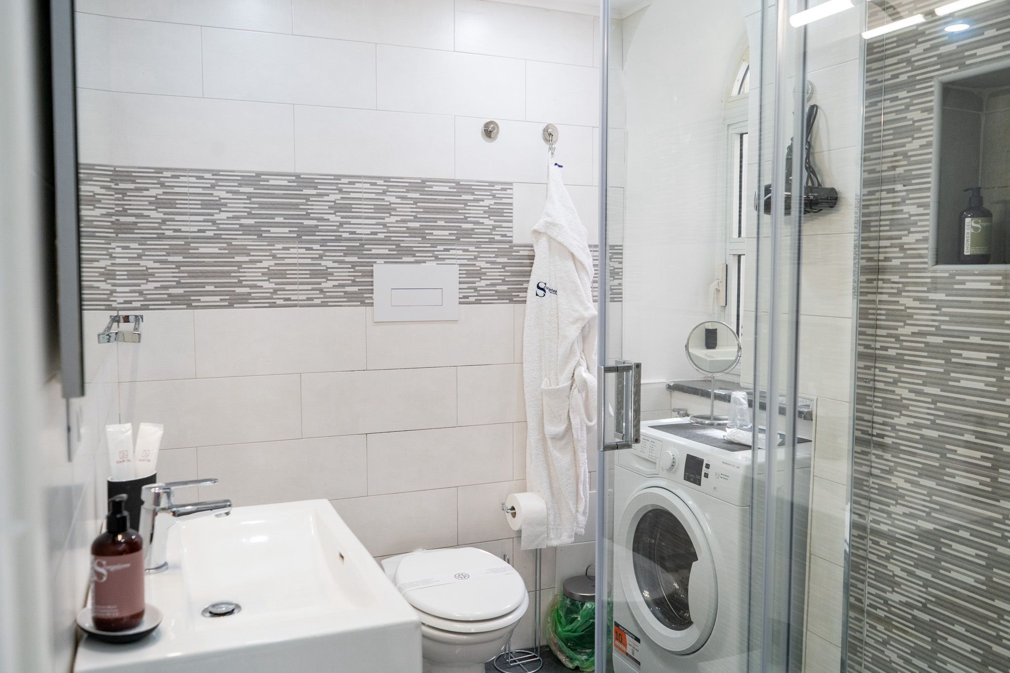 Une salle de bain moderne dotée d’une douche à parois de verre, d’un lave-linge encastré et de toilettes.