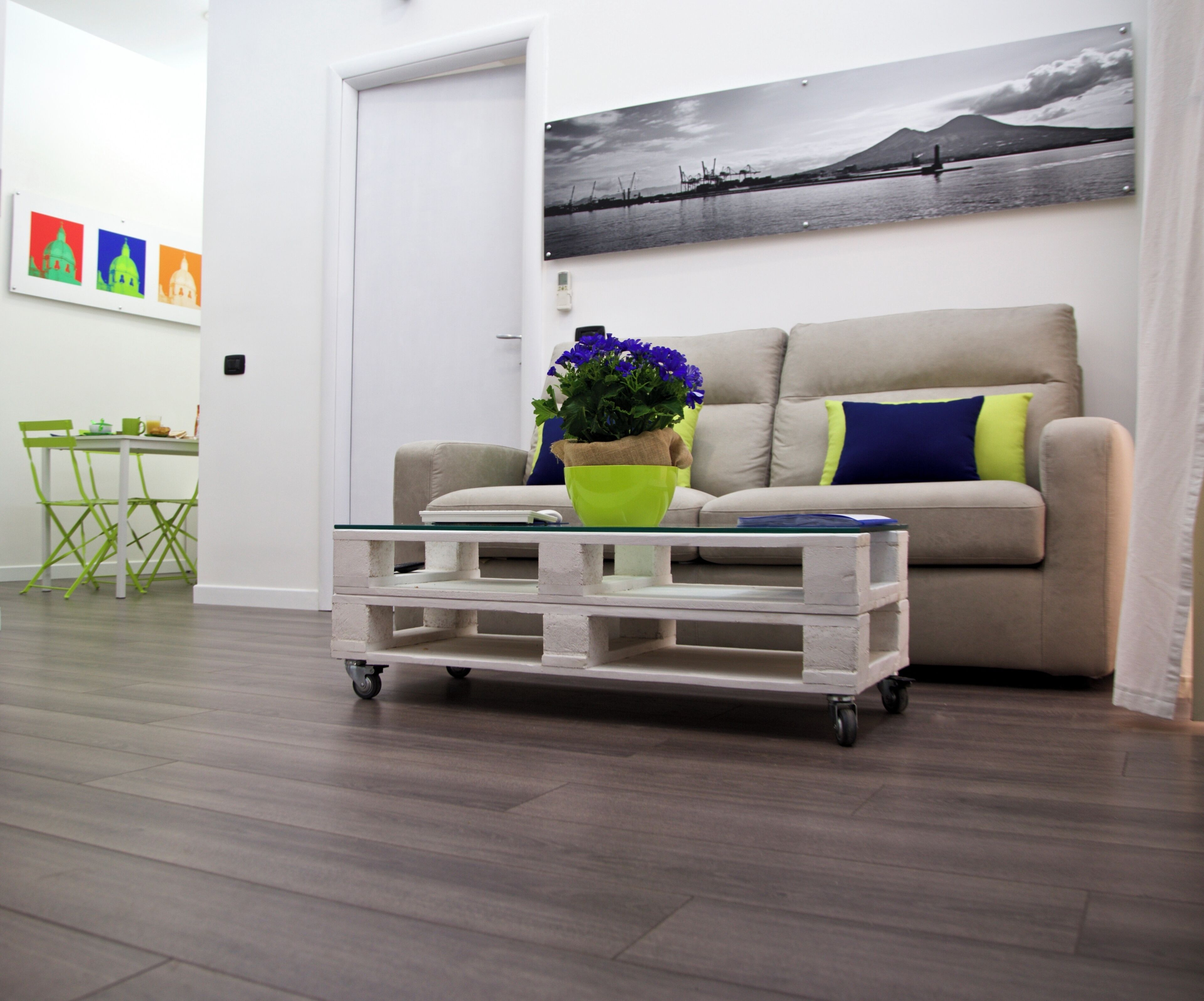 A living room with a sofa, a coffee table with wheels, a green chair, and a painting on the wall.