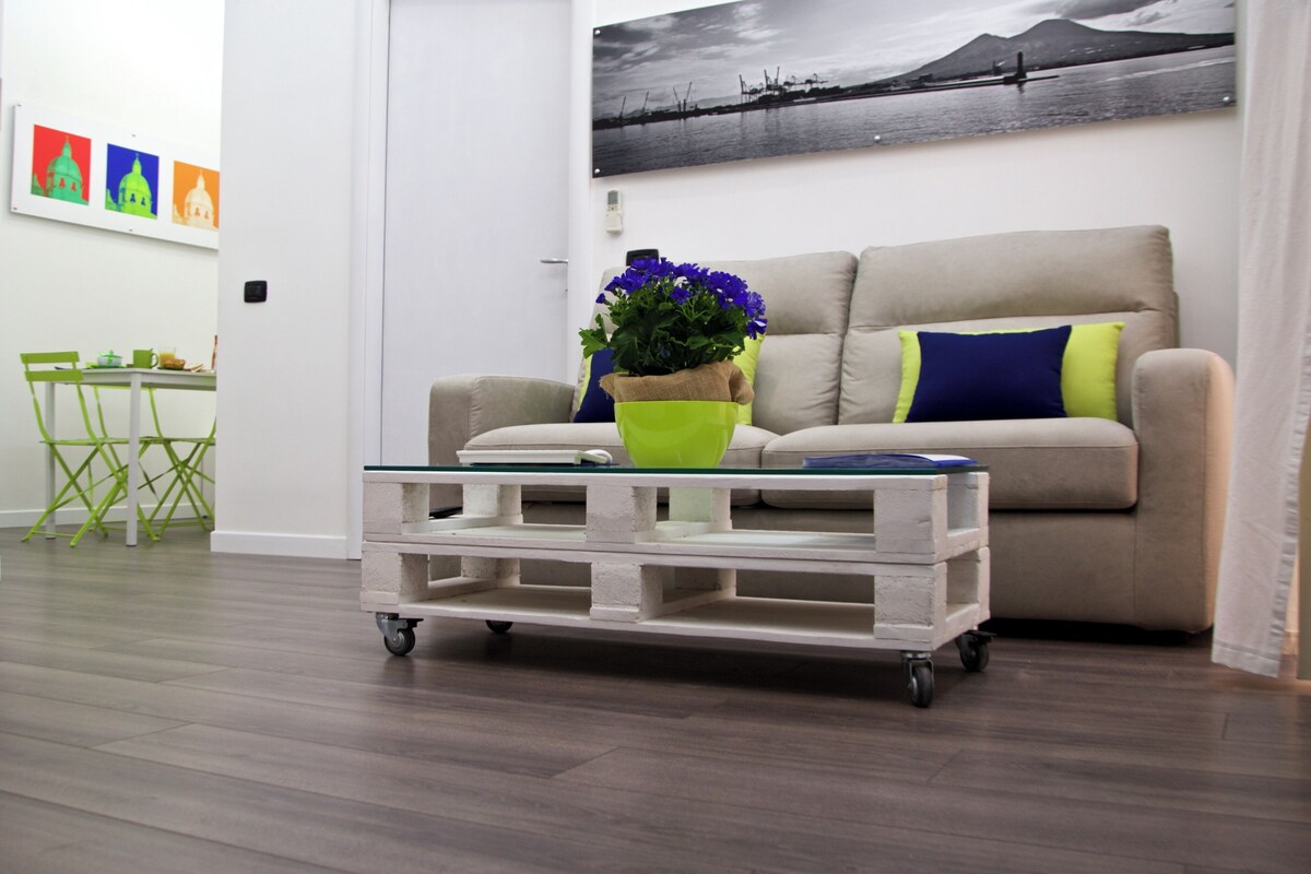 A living room with a sofa, a coffee table with wheels, a green chair, and a painting on the wall.