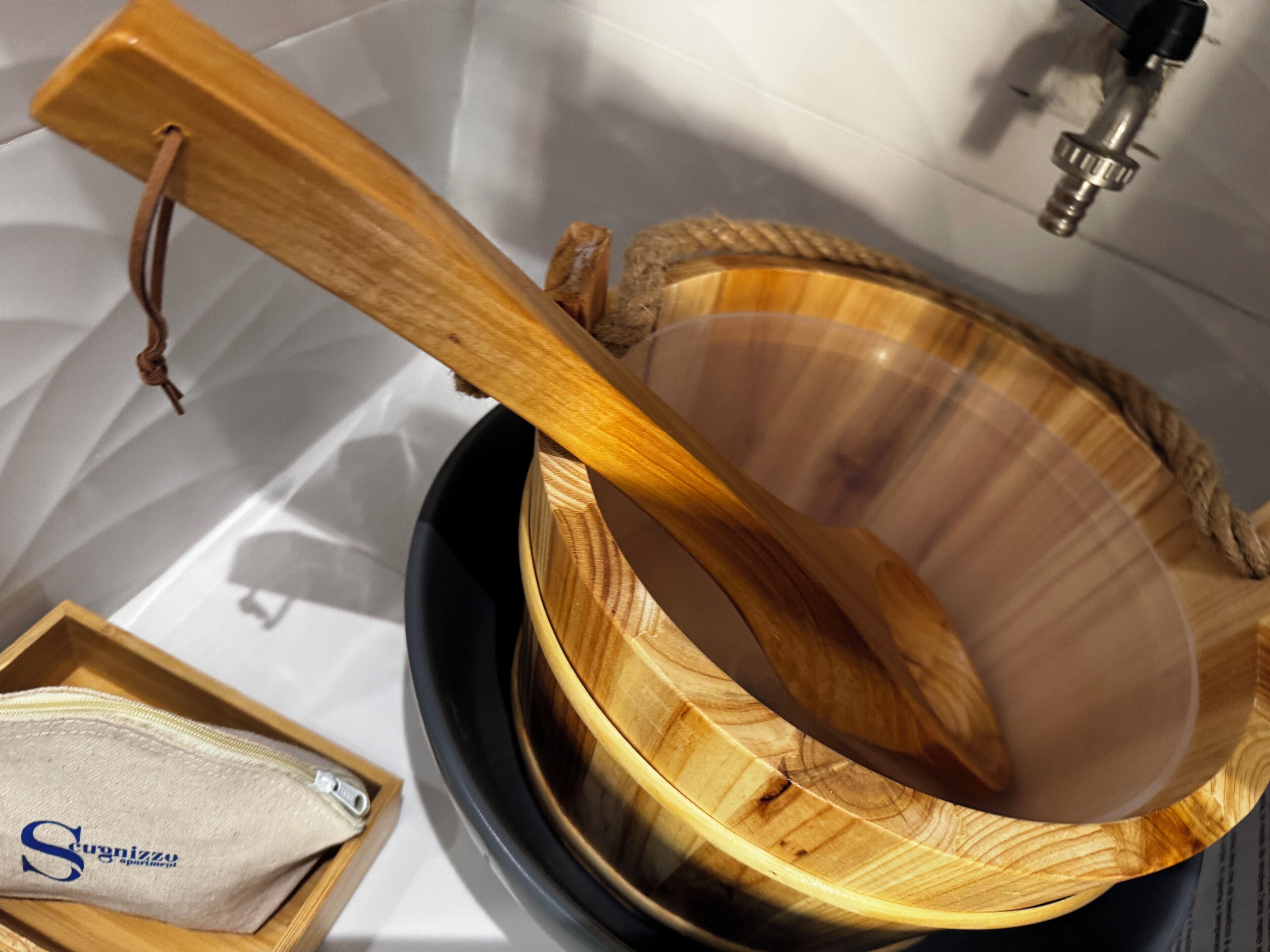 A wooden bowl with a rope handle, a small wooden box with a zipper, and a metal faucet in the background.
