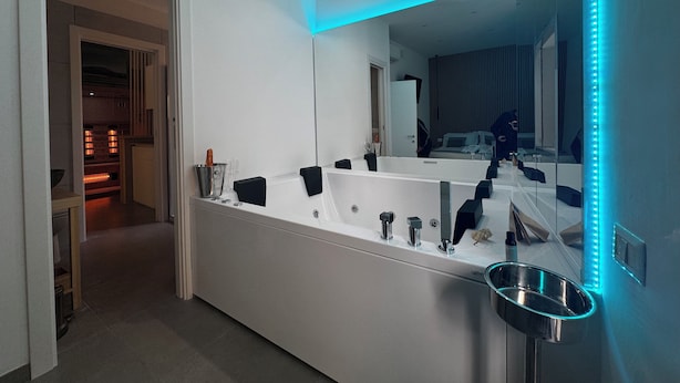 A modern bathroom with a large mirror, a bathtub, and a sink. There is a small metal bowl on the sink counter. - Scugnizzo Apartment (Naples)