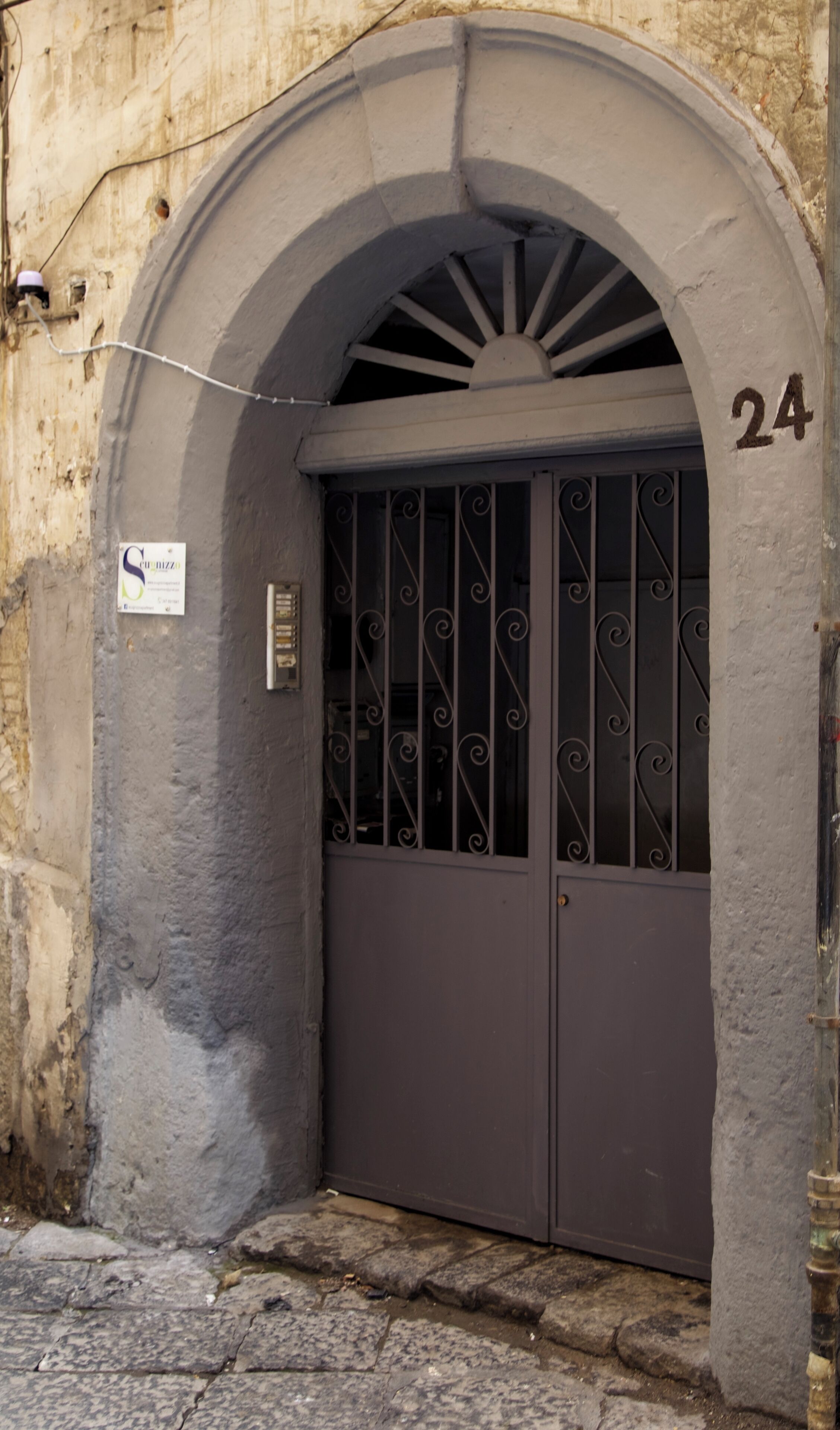 A building entrance with a metal gate, a sign indicating 'Caff. Bistrot', and the number '24' on the wall.