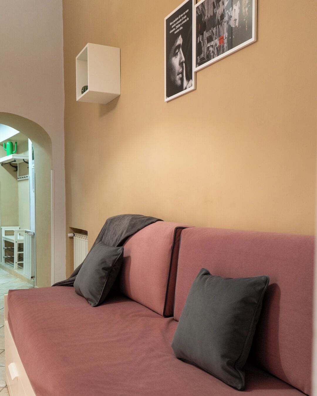 Una habitación con un sofá rosa, dos cojines negros, un estante blanco y dos cuadros en la pared.