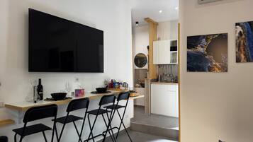A modern kitchen with a flat-screen TV, a dining area with four chairs, and a small bar area.