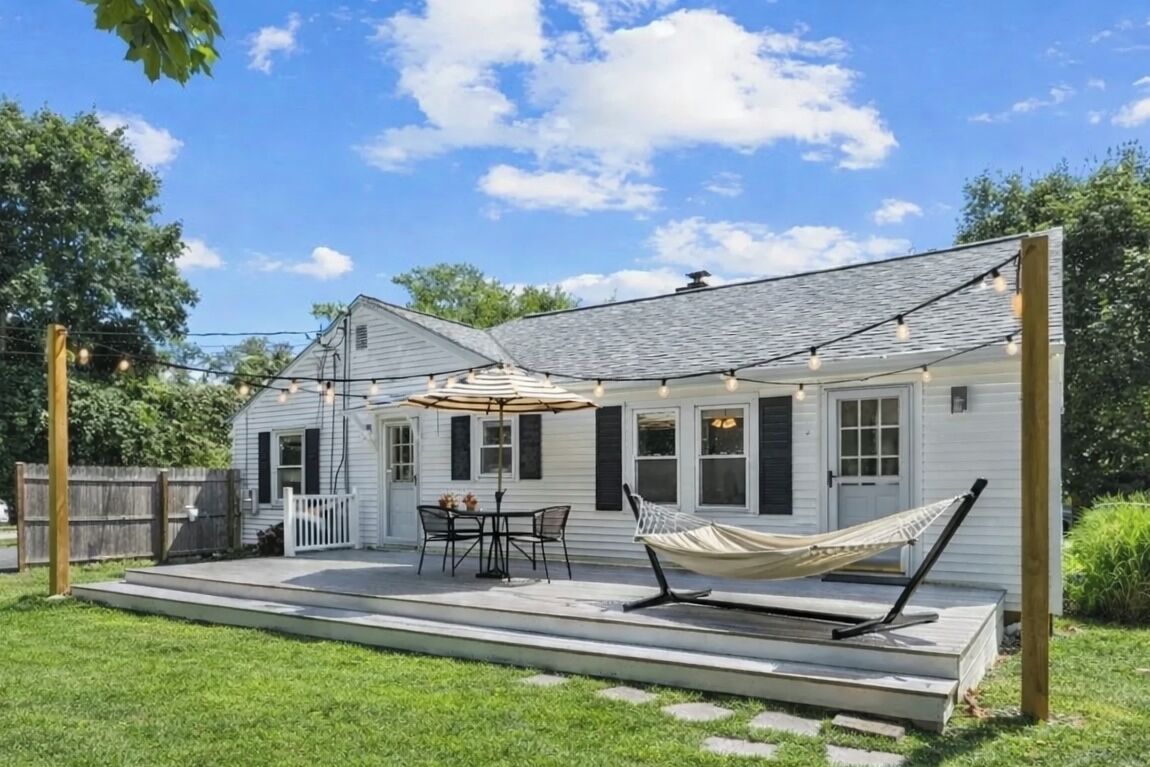Een huis met een overdekte veranda, tuinmeubilair en een hangmat.