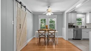 A kitchen with a dining table and chairs, a ceiling fan, and a view of the outdoors through the windows. - Narragansett Coastal Retreat- minutes to Beach & Pond (Narragansett)