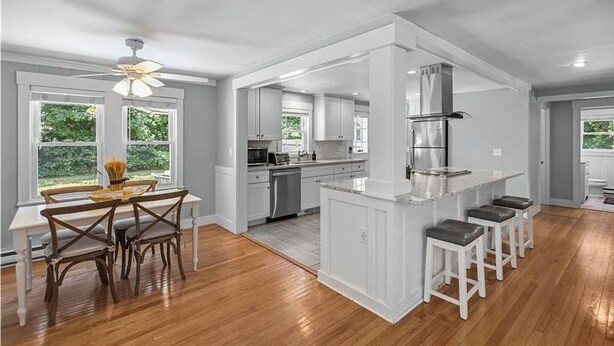 A spacious kitchen with a central island, white cabinetry, and a dining area with a wooden table and chairs. - Narragansett Coastal Retreat- minutes to Beach & Pond (Narragansett)