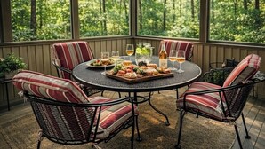 A covered patio with a round table, chairs, and a view of a forest.