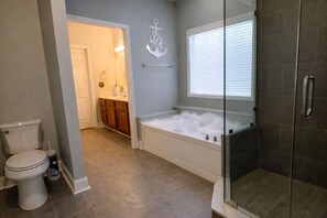 Un baño con inodoro, bañera llena de burbujas, zona de ducha y tocador con espejo.
