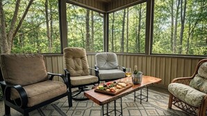 A covered porch with four chairs, a wooden table with a fruit platter, and a bottle of wine.