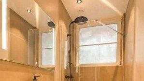 Ein modernes Badezimmer mit einem großen Spiegel, einer Dusche und einem Waschtisch mit Spüle und Handtuch.