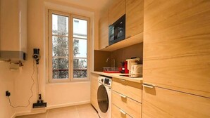 Eine kompakte Küche mit Einbauwaschmaschine, einer Mikrowelle und einem Fenster mit Blick auf Bäume.