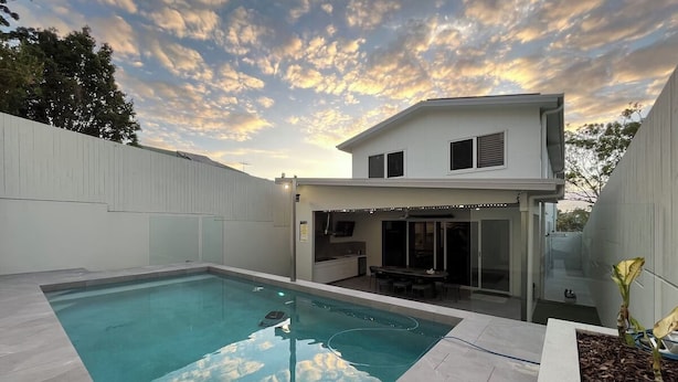 Una casa moderna con piscina, un patio cubierto y una estructura de dos pisos.