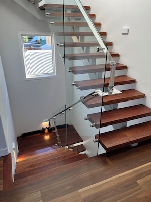 A modern staircase with glass railings and wooden steps. - Charming 3-bedroom house in beautiful Manly with AC (Manly)